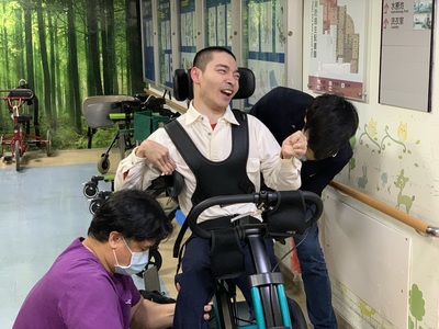 職能治療師陳柏佑(左)協助有高張力的院生小傑坐上復健三輪車